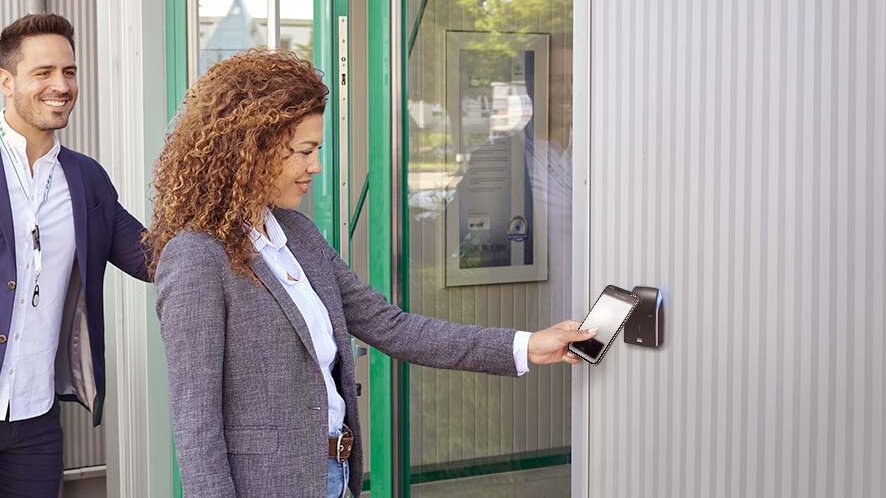 A mobile phone is held in front of a reader for access control to open a door.