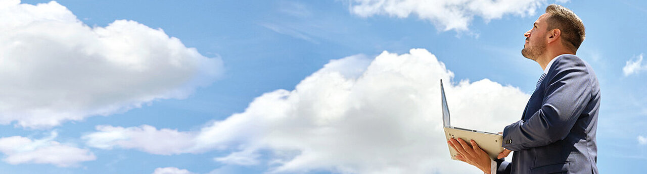 Mann mit Laptop schaut in Wolkenhimmel hoch
